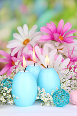 Easter candles with flowers on bright background