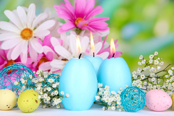 Easter candles with flowers on bright background