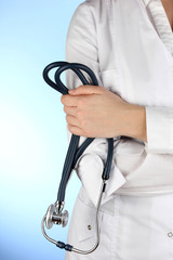 Doctor with stethoscope in hands on blue background
