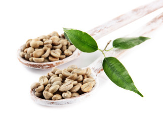 Green coffee beans in wooden spoons and leaves isolated on