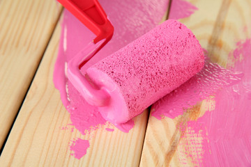 Obraz na płótnie Canvas Paint roller brush with pink paint, on wooden background