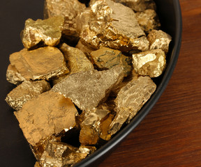 Gold pan with golden nuggets inside on wooden background