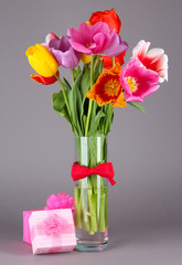 Beautiful tulips in bouquet with gifts on gray background