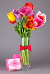 Beautiful tulips in bouquet with gifts on gray background