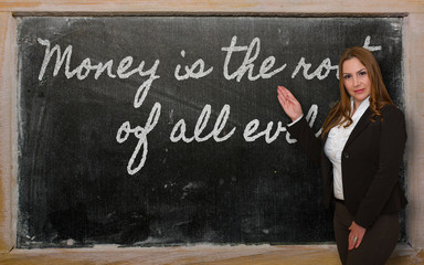 Teacher showing Money is the root of all evil on blackboard