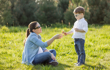 Naklejka na ściany i meble Son giving a bouquet of flowers to his pregnant mother in a fiel