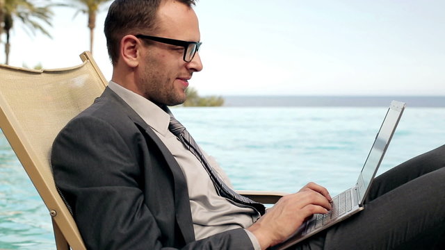 Businessman working on laptop in tourist resort, steadicam shot