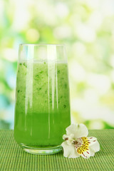 Glass of cucumber juice, on bamboo mat, on green background