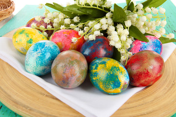 Easter eggs on wooden plate on napkin with flowers close-up