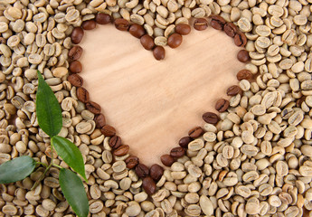 Green and brown coffee beans with leaves on wooden background