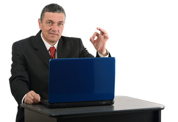 Aged businessman sitting at desk with a laptop isolated on white