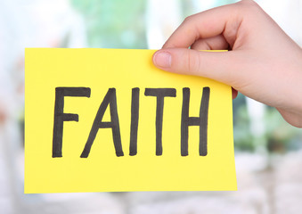 Faith word on piece paper in hand on window background