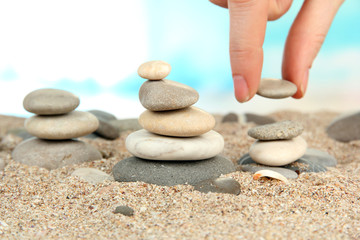 Fototapeta na wymiar Hand builds tower of sea stones on sand on bright background