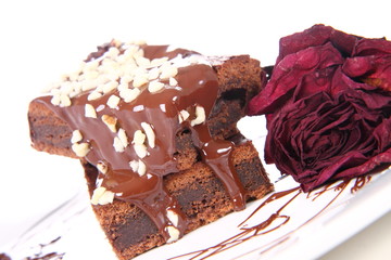 Slices of a brownie on white coverd with chocolate and nuts
