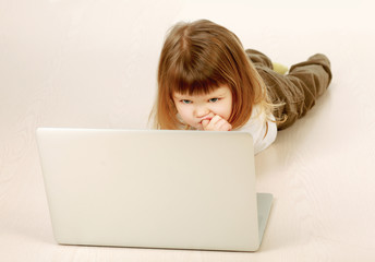 A little girl with a laptop lying on the floor