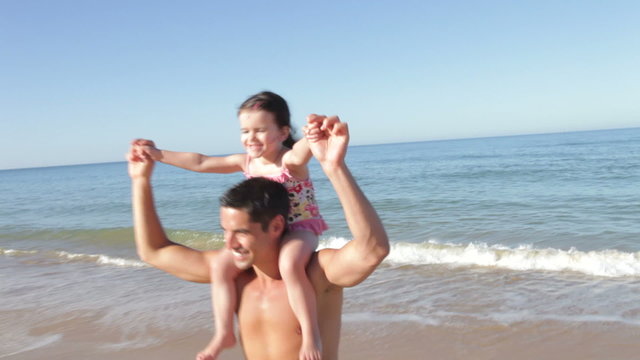 Father Carrying Daughter On Shoulders As They Run Out Of Sea