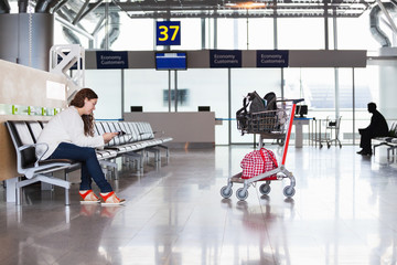 Woman waiting flight in airport lounge with luggage hand-cart