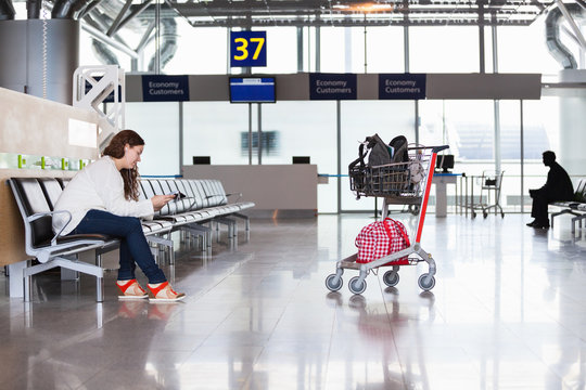 Woman waiting flight in airport lounge with luggage hand-cart