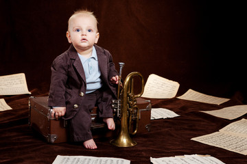 Caucasian baby boy plays with trumpet between sheets with musica