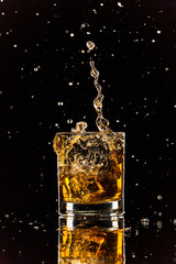 Whiskey splashing out of glass on black background