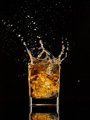 Whiskey splashing out of glass on black background