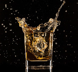 Whiskey splashing out of glass on black background