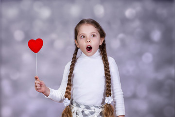 Surprised little girl with heart on a stick