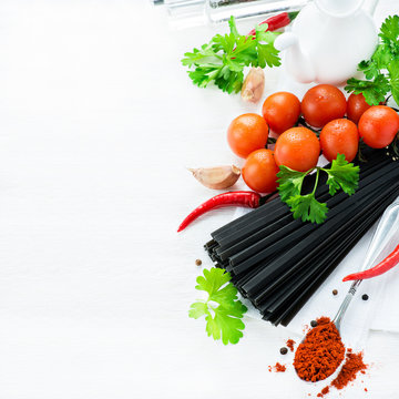 Uncooked black pasta with tomatoes, herbs, spices  and oil jug