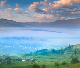 Summer landscape with a mountain village in the mist