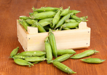 Green peas in crate on wooden background