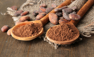Cocoa powder in spoons and beans on wooden background