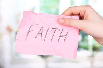 Faith word on piece paper in hand on window background