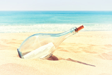 A bottle with a letter of distress in the sand on the beach. In