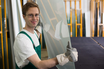 Glazier handling piece of glass in workshop