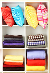 Bright pillows, towels and plaids on shelves, isolated on white