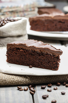 Chocolate cake on white plate, on hessian. Coffee beans on woode