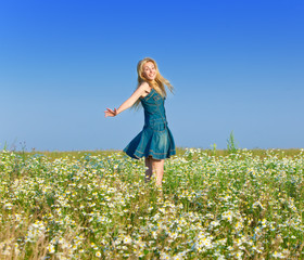 Naklejka na ściany i meble The beautiful happy young woman in the field of chamomiles