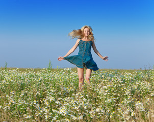 Naklejka na ściany i meble The happy young woman jumps in the field of chamomiles