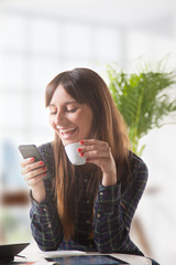 Smiling young woman with a coffee and send a message