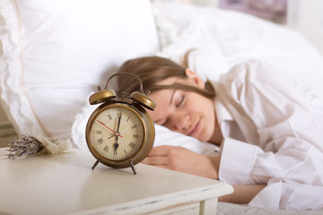 Alarm clock on table and woman sleeping