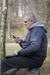 Man with cell phone, PC on a bench near river in park
