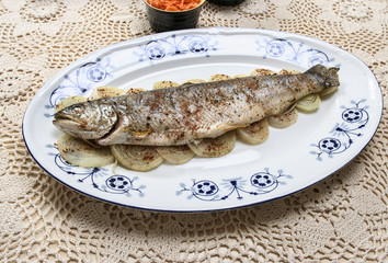 Fish plate in greek tavern. Roasted trout on onion.