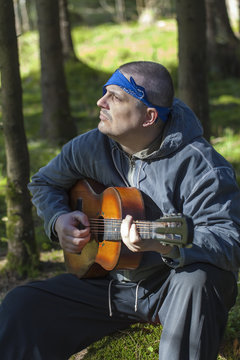 Man sitting on a stump and playing guitar in the woods