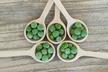 Frozen green peas on wooden spoons, close up