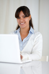 Young woman looking at you while working on laptop