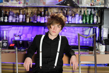 Fototapeta na wymiar Glamorous boy in black shirt and white suspenders sits near bar