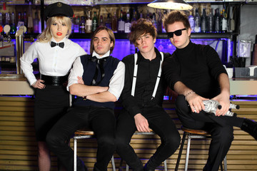 Four young rock band in black and white pose near bar counter.