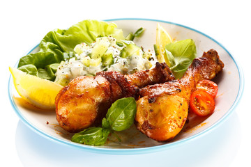 Grilled chicken legs and vegetables on white background