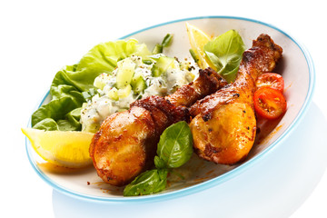 Grilled chicken legs and vegetables on white background
