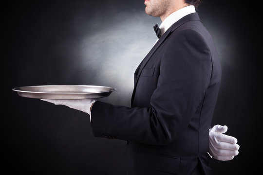 Waiter holding empty silver tray over black background